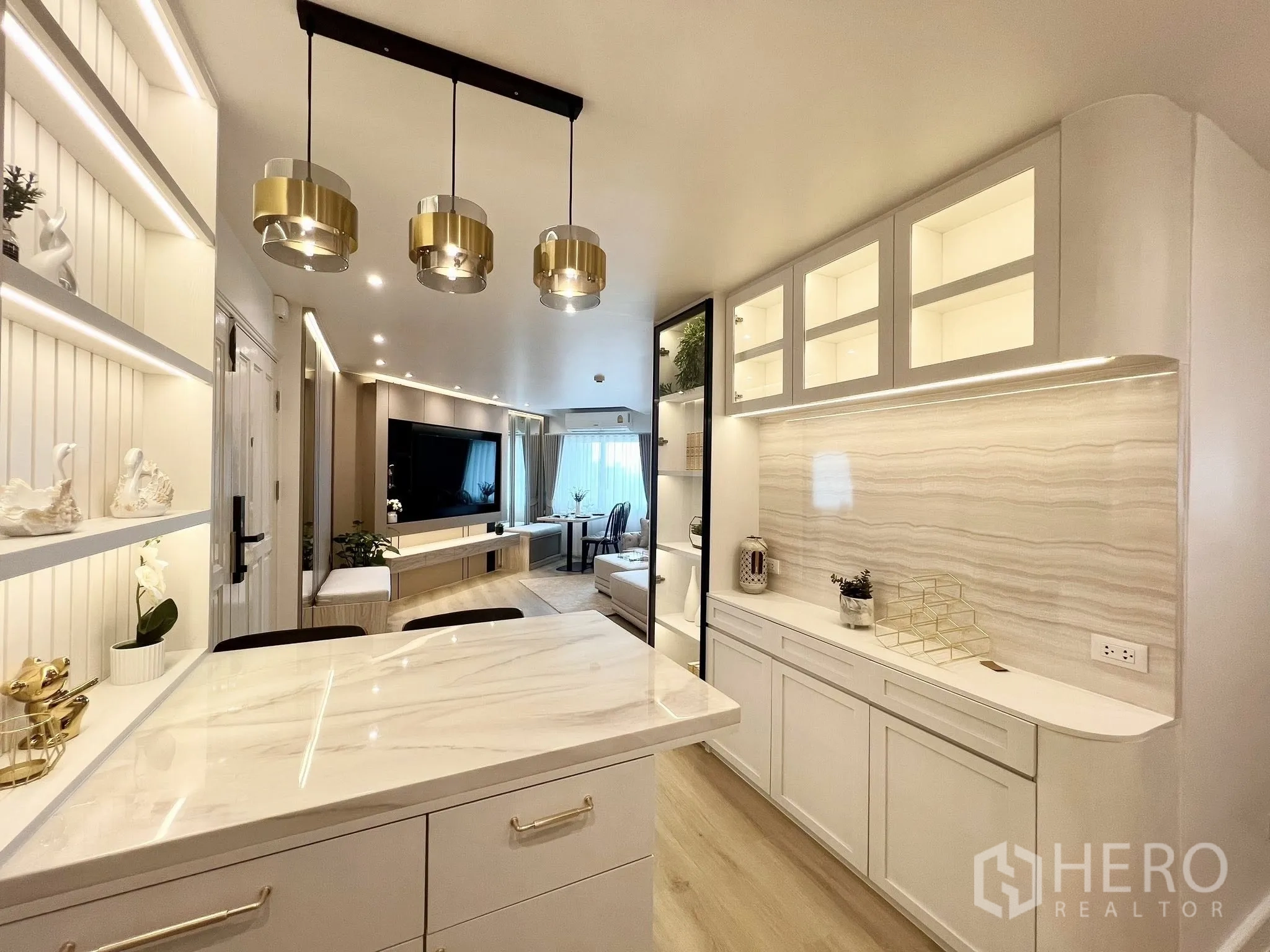 Condominium for rent or sale in Yan Nawa, Bangkok - Kitchen perspective to living room featuring marble island, gold pendant lights and illuminated display shelving.