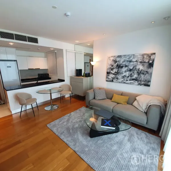Condominium for rent in Watthana, Bangkok - Bright open-plan living room with grey sofa, glass coffee table, wood floors and a compact kitchen.
