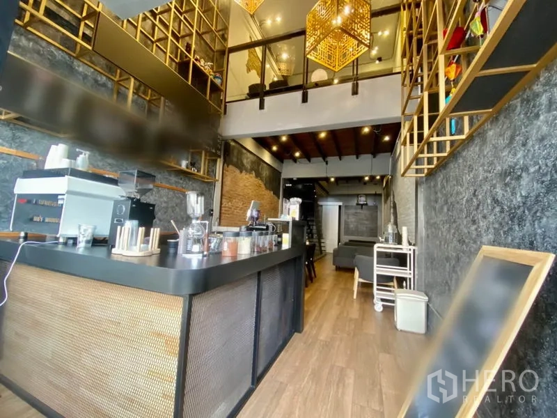Shophouse for rent in Pathum Wan, Bangkok - Loft-style shophouse interior with espresso bar, wood floors, mezzanine with glass railing and gold lattice shelving.