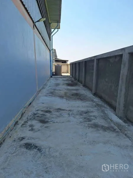 Warehouse for sale in Pathum Thani - Side service walkway with concrete surface along the boundary wall of the building.