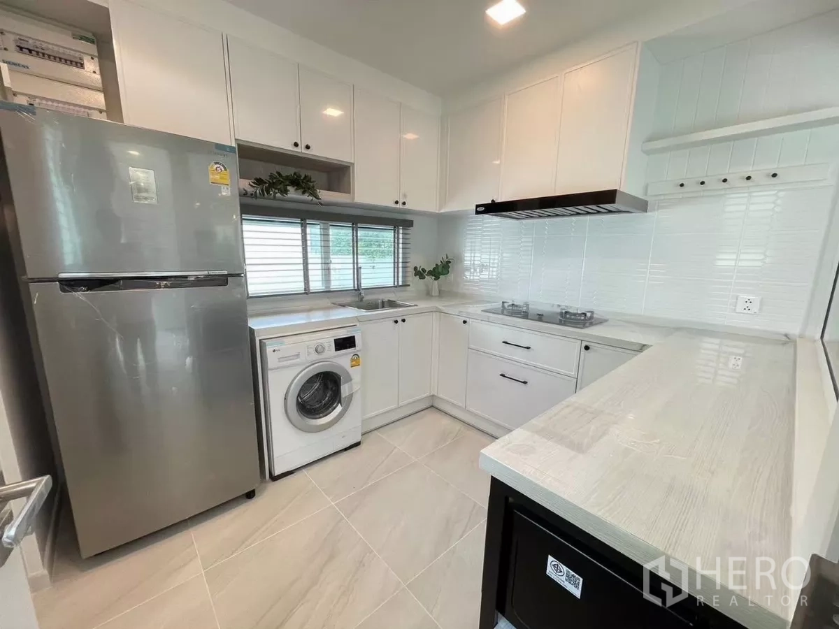 Detached House for rent in Bang Phli, Samut Prakan - U-shaped white kitchen with refrigerator, washing machine, gas hob, and sink.