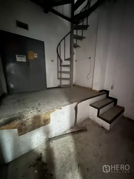 零售空间 出租在Watthana, Bangkok - 金属旋转楼梯与抬高平台，旁有灰色服务门。