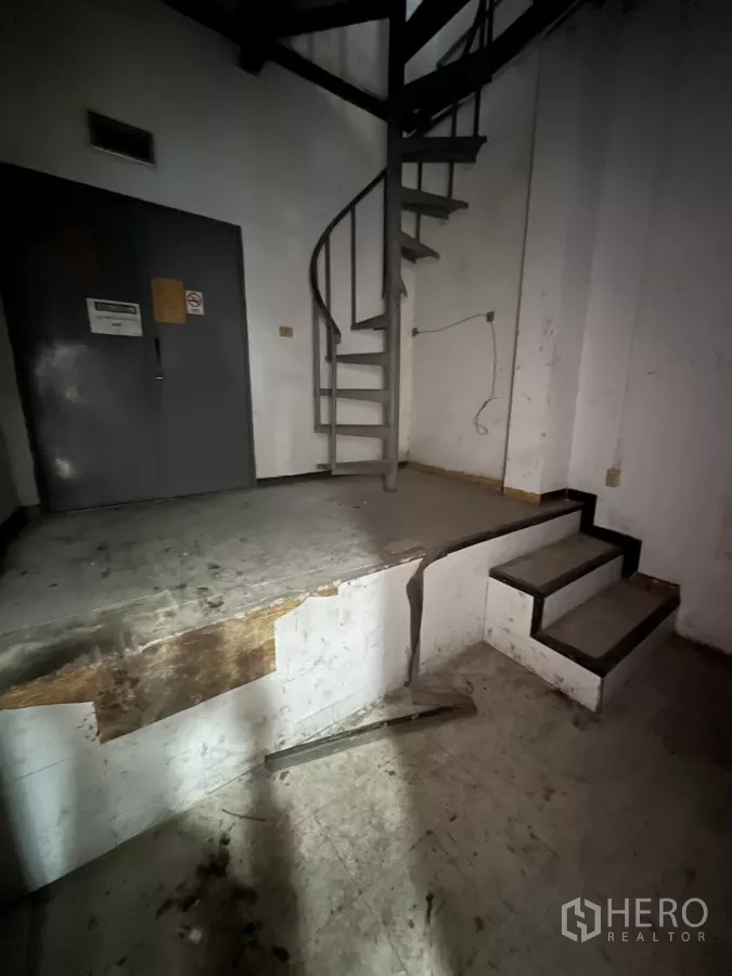 零售空间 出租在Watthana, Bangkok - 金属旋转楼梯与抬高平台，旁有灰色服务门。