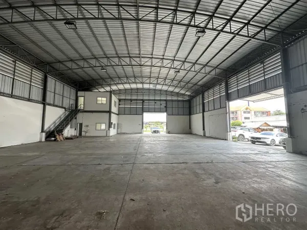 Factory for rent in Pathum Thani - Open-plan factory hall facing a large loading door with on-site parking outside.