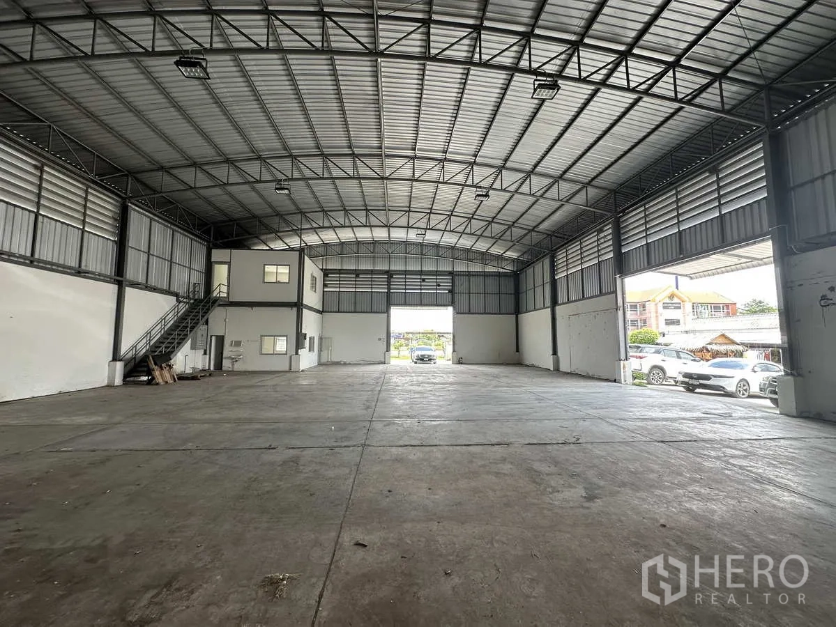 Factory for rent in Pathum Thani - Open-plan factory hall facing a large loading door with on-site parking outside.