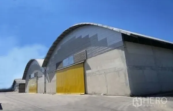 Warehouse for rent in Phra Pradaeng, Samut Prakan - Modern arched-roof concrete warehouse blocks with yellow sliding doors on a clear day.