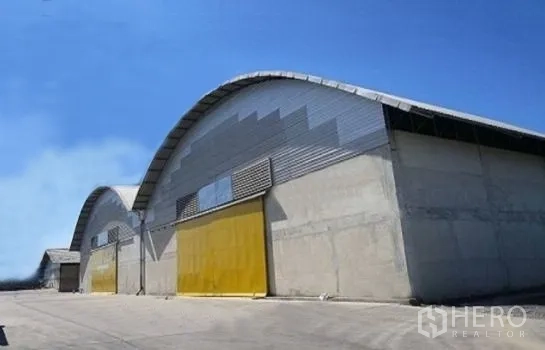 Warehouse for rent in Phra Pradaeng, Samut Prakan - Modern arched-roof concrete warehouse blocks with yellow sliding doors on a clear day.