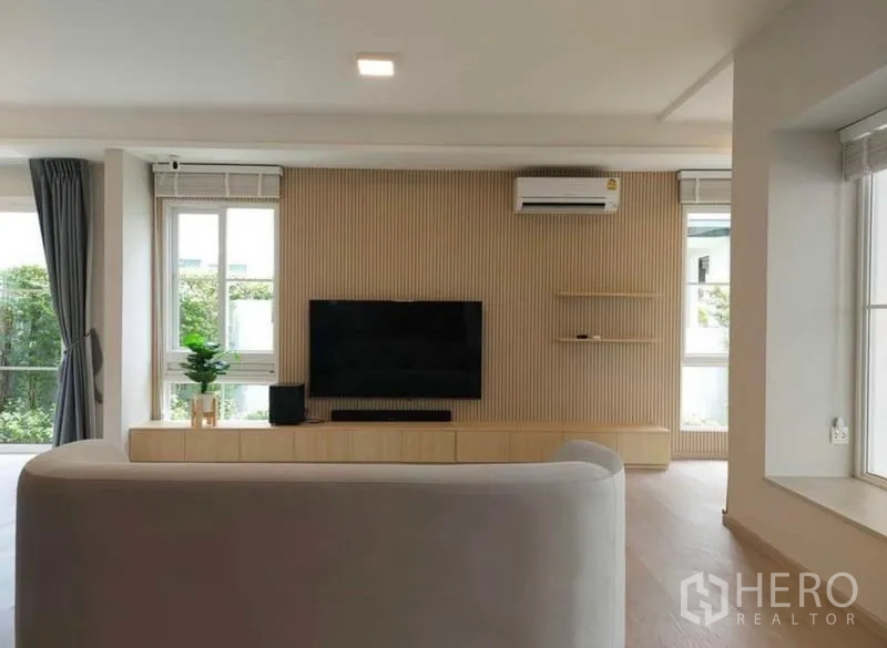 Detached House for rent in Prawet, Bangkok - Living room media wall with mounted TV, built-in console, air conditioner, and natural light.