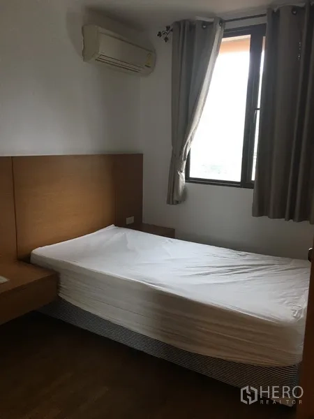 Condominium for rent in Pathum Wan, Bangkok - Cozy second bedroom with single bed, curtained window and wall-mounted air conditioner.