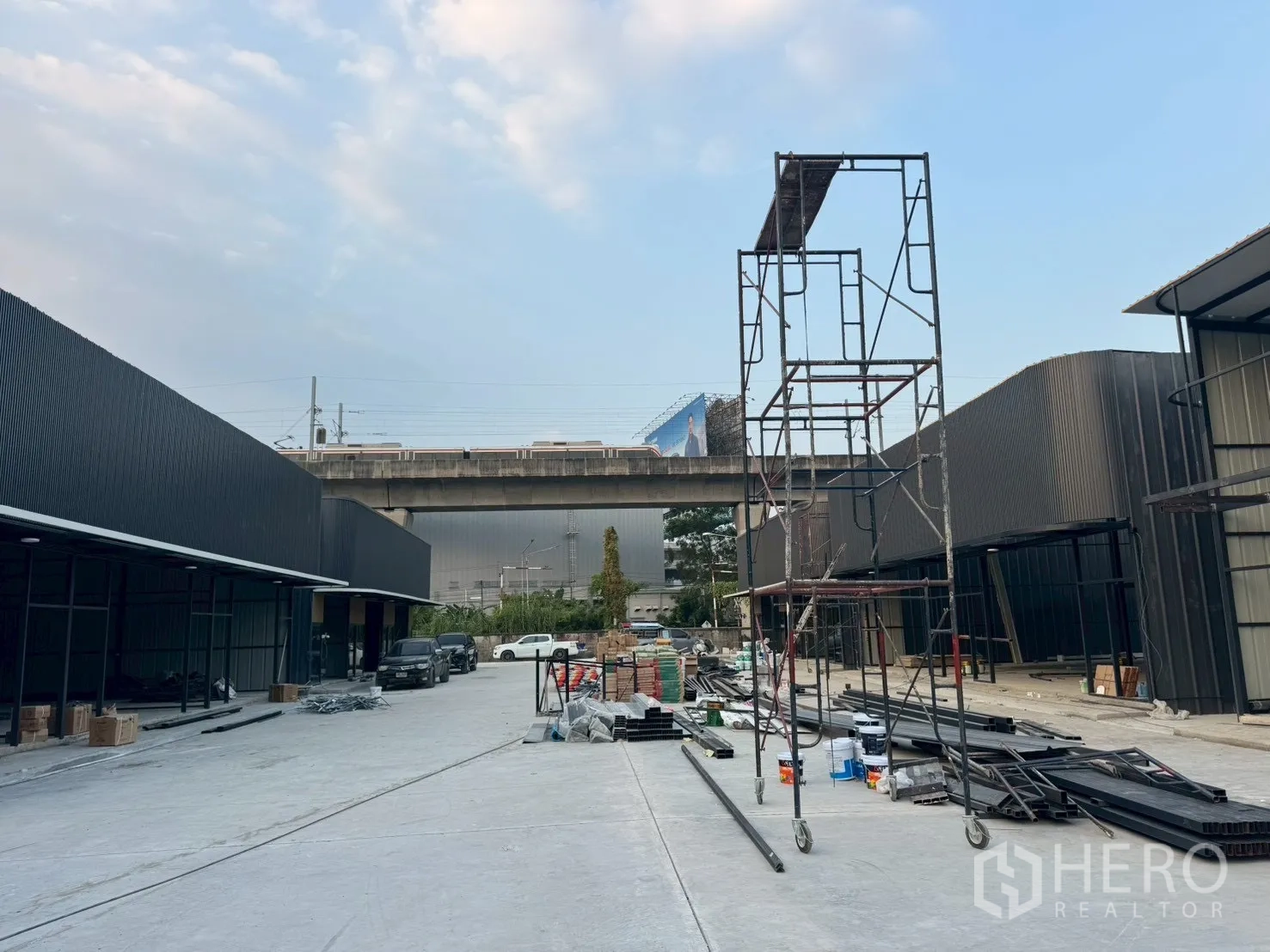 Warehouse for rent in Suan Luang, Bangkok - Central service lane between warehouse blocks with scaffolding and materials, rail viaduct in the background.