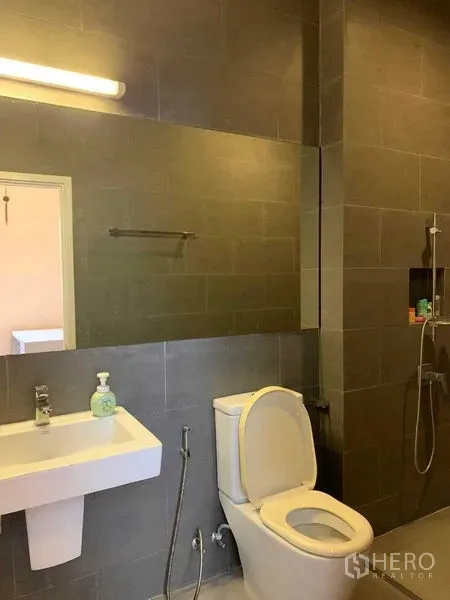 联排别墅 出租在Khan Na Yao, Bangkok - 灰色瓷砖浴室，超大镜面、马桶、洗手盆与淋浴区。