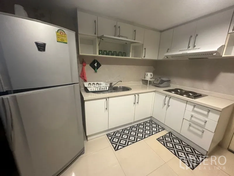 Condominium for rent in Watthana, Bangkok - Bright U-shaped kitchen with white cabinets, stovetop, range hood and a large fridge.