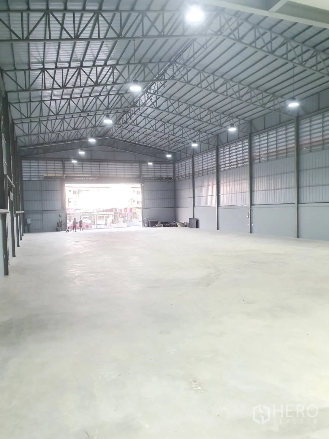 货栈 出租在Sai Mai, Bangkok - 仓库中央通道延伸至出入口，山墙钢结构屋顶与高位灯具。