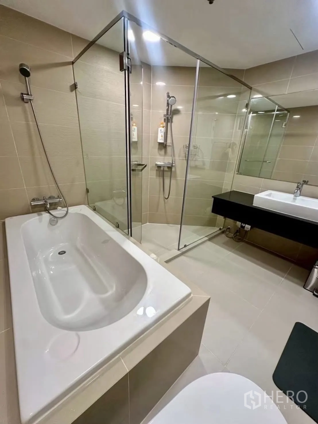 Condominium for rent in Huai Khwang, Bangkok - Modern bathroom with bathtub, glass shower, and vanity.