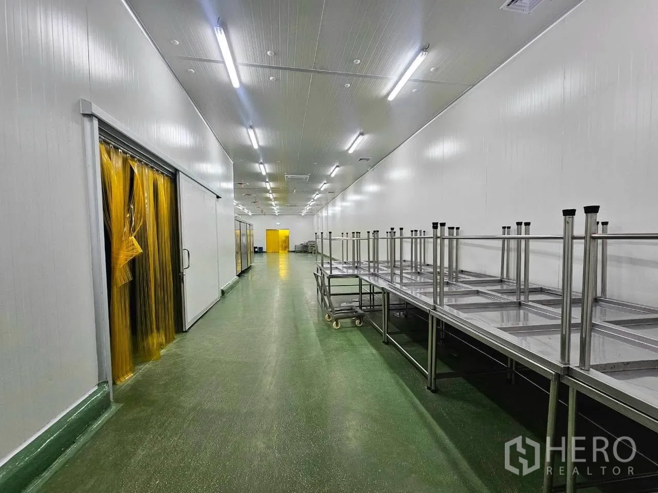 工厂 for rent in Mueang Samut Sakhon, Samut Sakhon - 绿色地面走道，不锈钢工作台与黄色软帘。