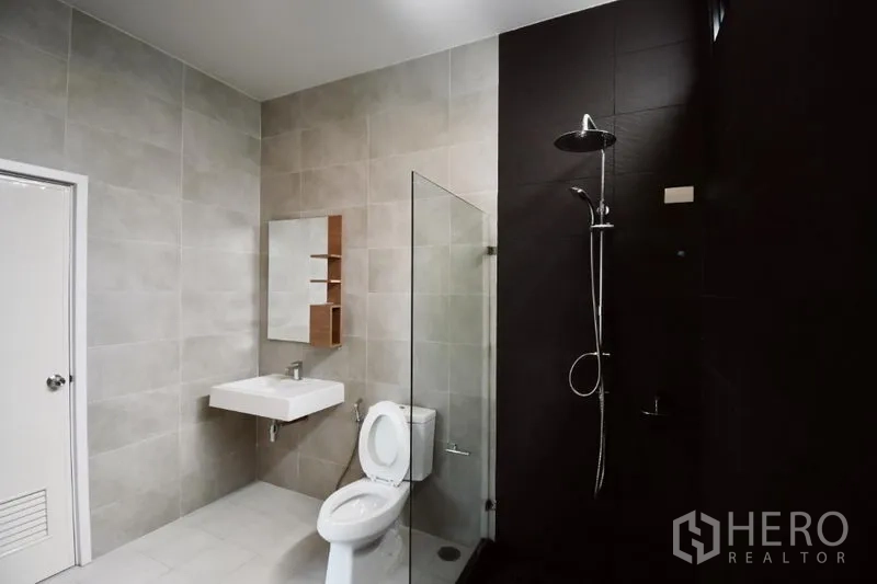 Detached House for rent in Prawet, Bangkok - Contemporary bathroom with glass-enclosed rain shower, toilet, and gray wall tiles.
