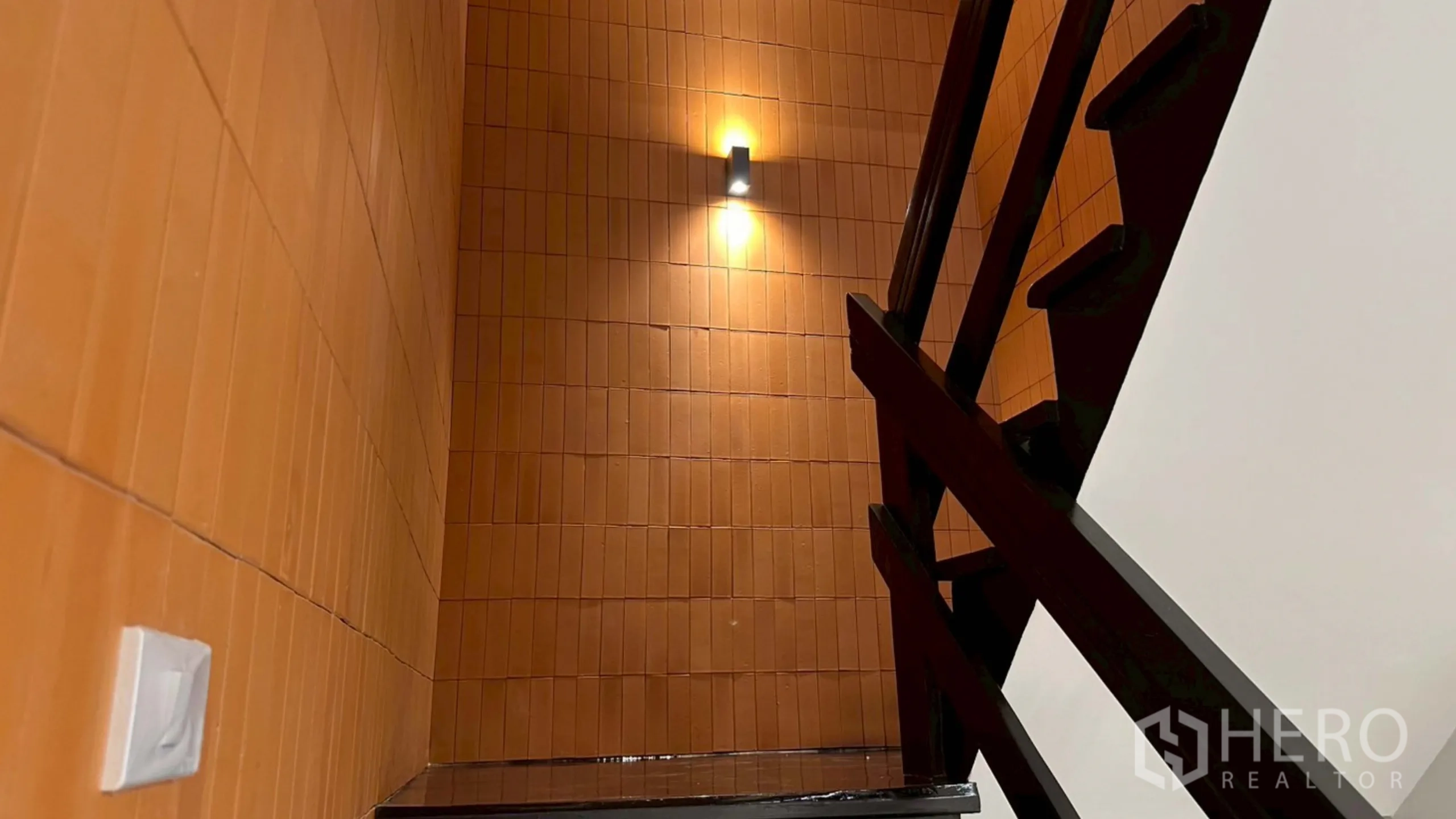 Home Office for rent in Watthana, Bangkok - Close-up of black stair handrail against orange tiled wall.