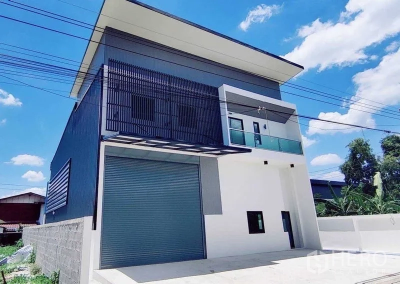 Warehouse for rent in Lam Luk Ka, Pathum Thani - Modern two-story warehouse exterior in Lam Luk Ka with large roller shutter, balcony and canopy.