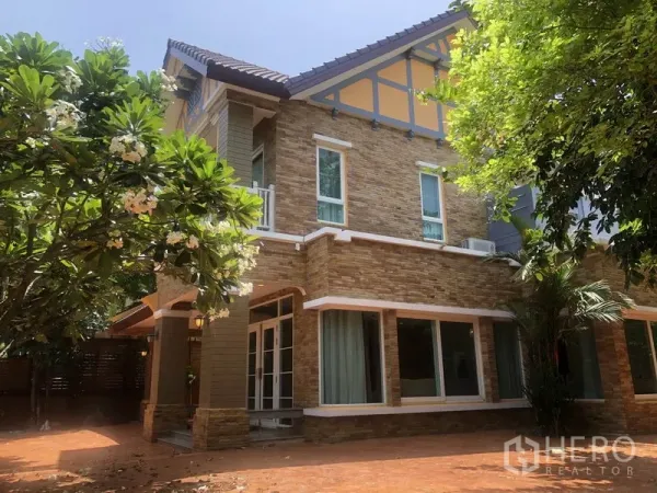 独立式住宅 出租或出售在Pak Kret, Nonthaburi - 两层独栋别墅外观，石材立面与大窗，庭院绿树成荫