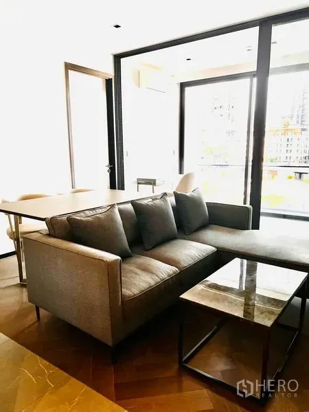 公寓 出售在Watthana, Bangkok - 客餐厅一体，灰色沙发、大理石茶几与餐桌，落地窗连通阳台。