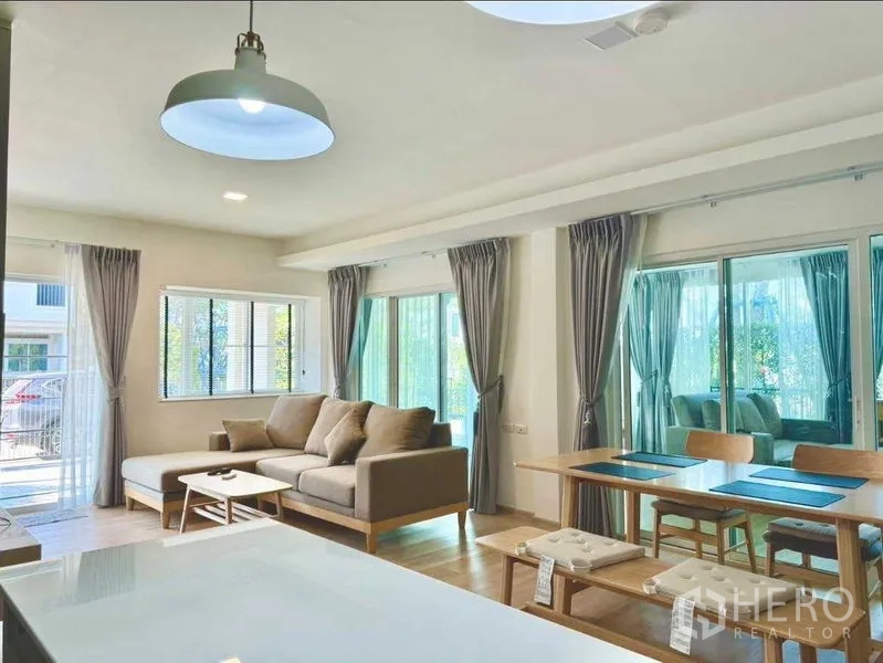 联排别墅 出租或出售在Prawet, Bangkok - 充满采光的起居与餐区，三面大窗与推拉门配灰色窗帘。