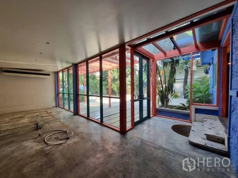 Detached House for rent in Khlong Toei, Bangkok - Glass-walled room with red frame doors opening to covered deck and garden.