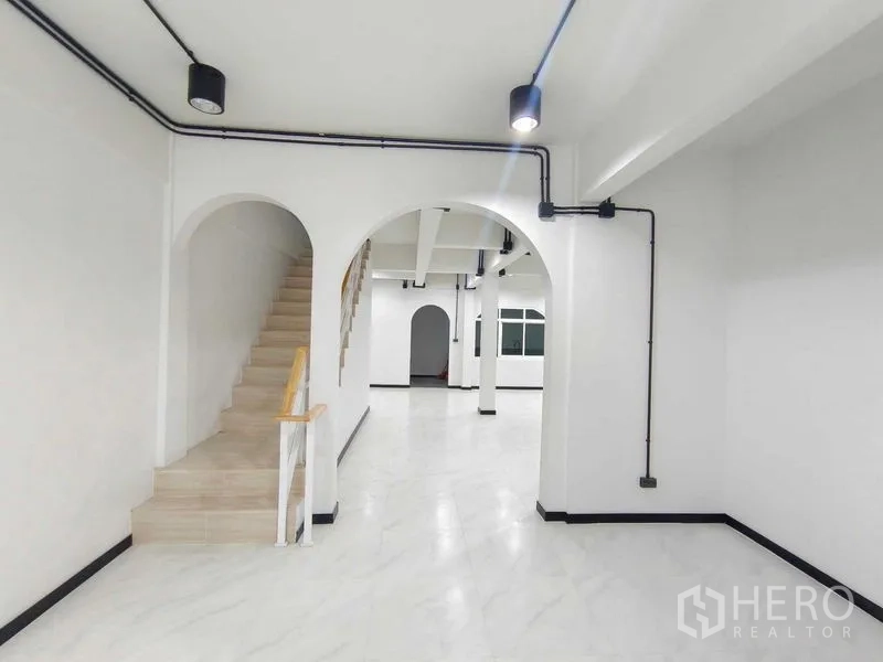 Townhouse for sale in Bang Phlat, Bangkok - Arched corridor and stairwell with marble-look floors and black conduit lighting.