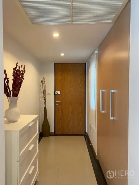 Condominium for rent or sale in Phra Khanong, Bangkok - Entrance hallway with wooden door, built-in wardrobes and white dresser under downlights.