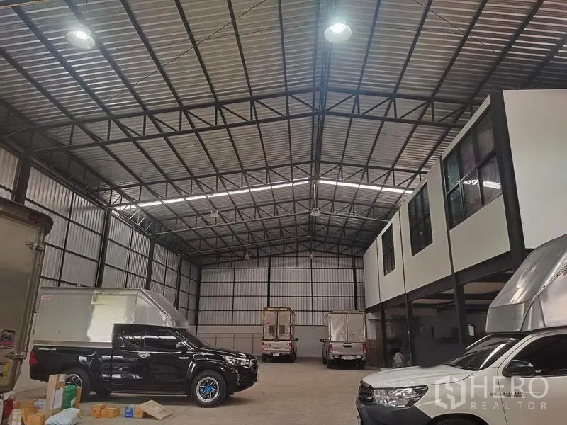 货栈 出租在Bang Khen, Bangkok - 夜间仓库内部，车辆与架空办公室位于钢结构屋顶下。