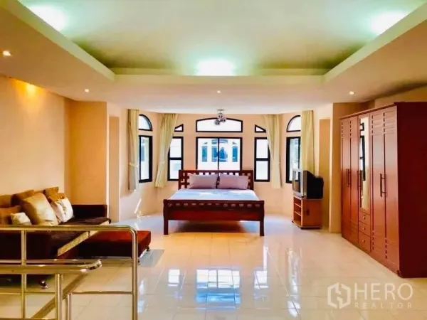 Townhouse for rent in Watthana, Bangkok - Spacious bedroom with wooden bed, sofa, wardrobe and arched windows in a bright tiled room.