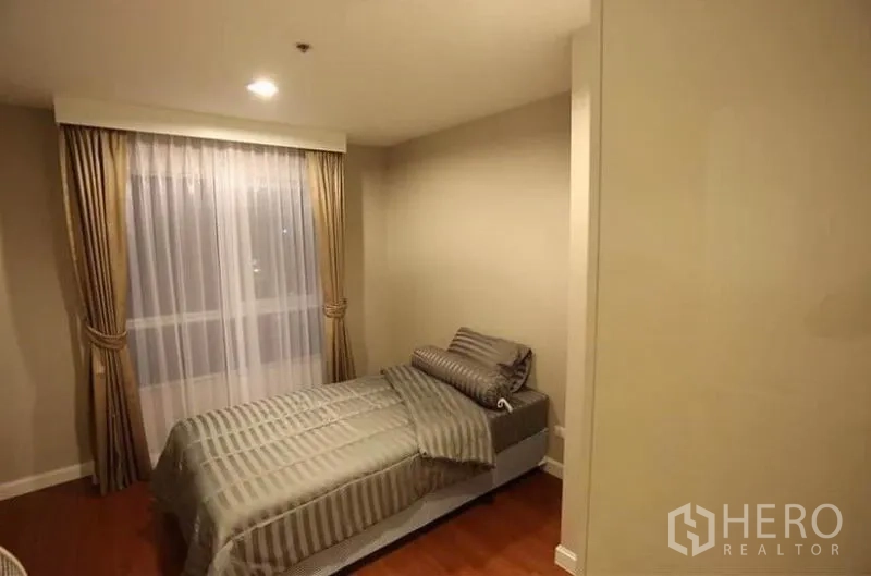 Condominium for rent in Huai Khwang, Bangkok - Second bedroom with single bed, draped window and wood flooring.