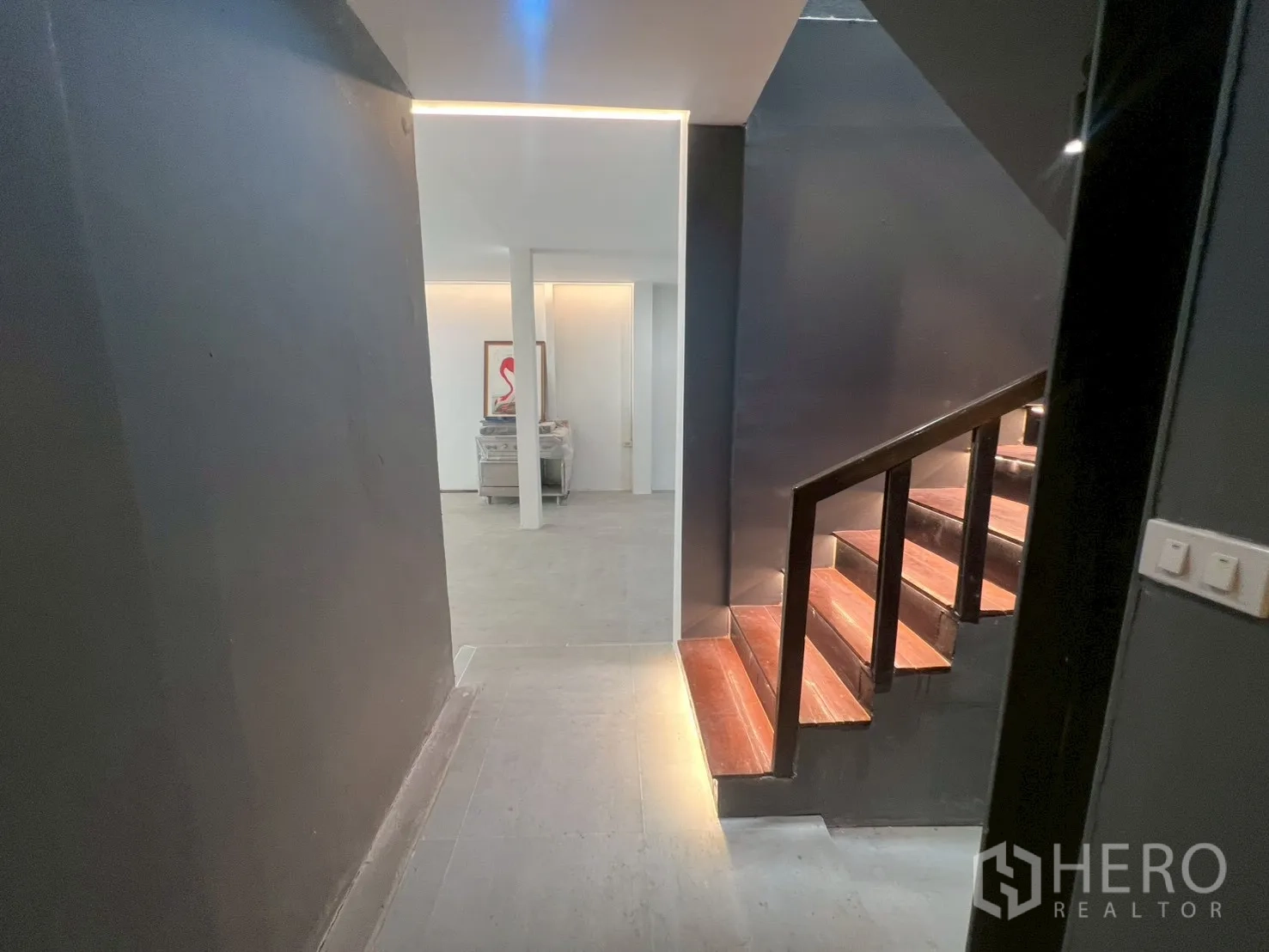 Home Office for rent in Watthana, Bangkok - Corridor with dark accent wall and a wooden staircase with step lighting.