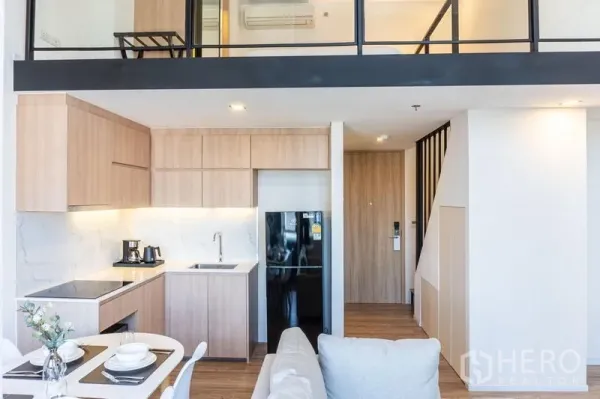 คอนโด ให้เช่าในKhlong Toei, Bangkok - มุมมองกว้างของครัว ตู้เย็นสีดำ และราวกันตกชั้นลอยเหนือห้องนั่งเล่น