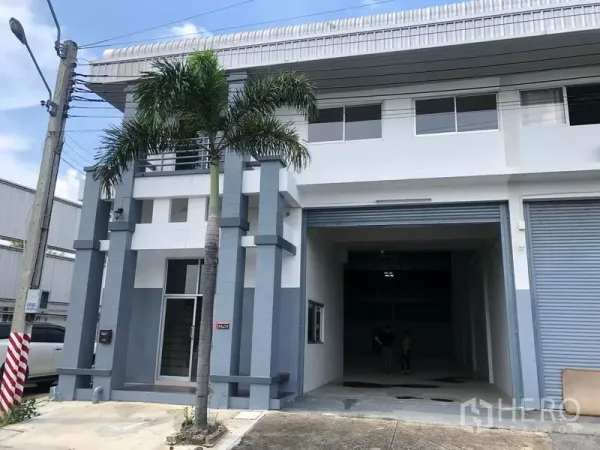 工厂 出租在Pak Kret, Nonthaburi - 暖武里府Pak Kret现代两层工厂外立面，配宽幅卷闸门与棕榈树。