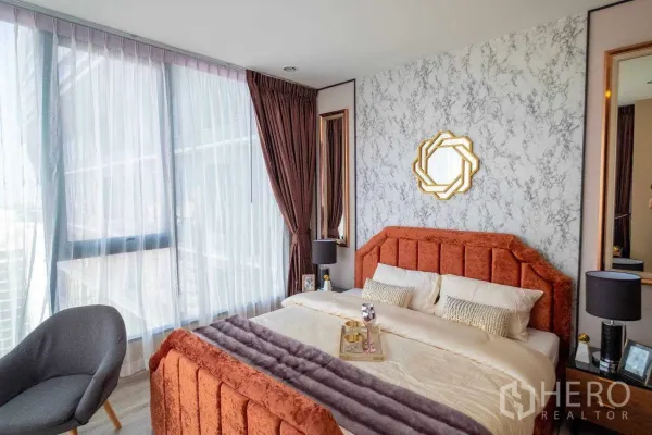 คอนโด ให้เช่าในBang Na, Bangkok - ห้องนอนมาสเตอร์รับแสงด้วยหน้าต่างเต็มบาน ผนังลายหินอ่อน และเตียงกำมะหยี่สีส้มในคอนโดบางนา