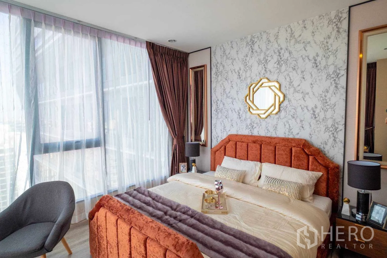 คอนโด ให้เช่าในBang Na, Bangkok - ห้องนอนมาสเตอร์รับแสงด้วยหน้าต่างเต็มบาน ผนังลายหินอ่อน และเตียงกำมะหยี่สีส้มในคอนโดบางนา