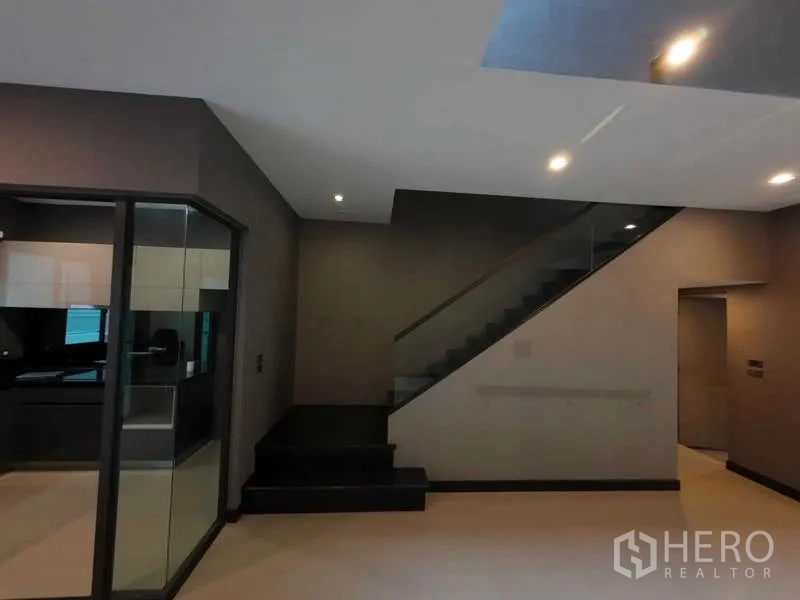 联排别墅 出租或出售在Lat Phrao, Bangkok - 带玻璃扶手的楼梯，旁有通往相邻房间的门。