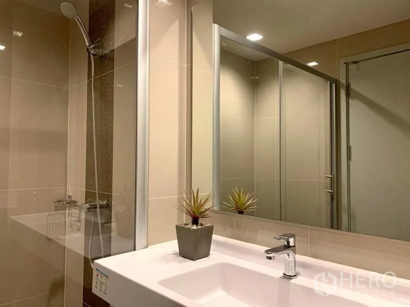 公寓 出租或出售在Phra Khanong, Bangkok - 现代浴室，超大镜面、白色台盆与玻璃淋浴间。