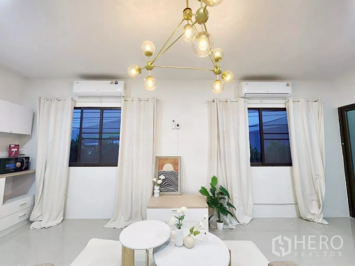 Detached House for rent in Chatuchak, Bangkok - Lounge area with modern pendant light, double windows, white curtains and split air-con units.
