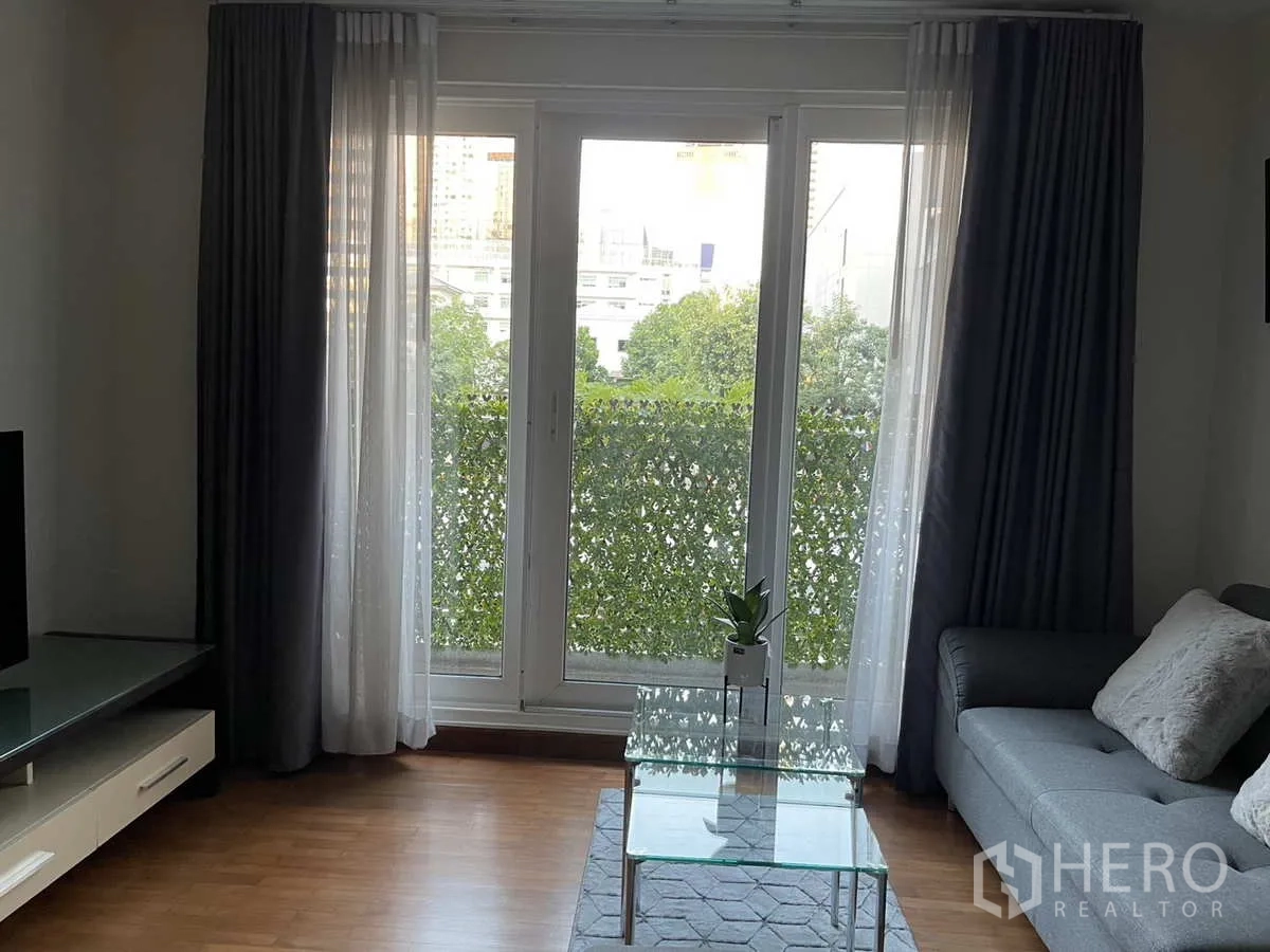 Condominium for rent in Watthana, Bangkok - Living area facing balcony with sheer and blackout curtains and TV unit.