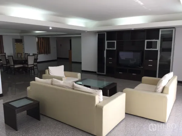 Condominium for rent in Watthana, Bangkok - Living room with built-in dark wood TV wall, beige sofas, and reflective tile flooring.