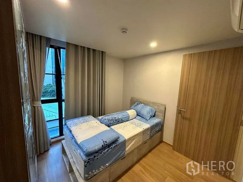 公寓 出租在Pathum Wan, Bangkok - 紧凑次卧，木地板，落地窗配窗帘与单人床。