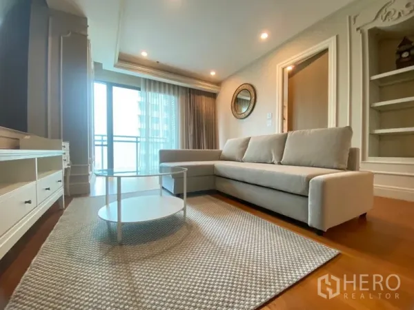 คอนโด ให้เช่าในKhlong Toei, Bangkok - พื้นที่นั่งเล่นสว่าง โซฟา L‑shape ประตูกระจกสูงจรดเพดานเชื่อมถึงระเบียงในคอนโดย่านคลองเตย