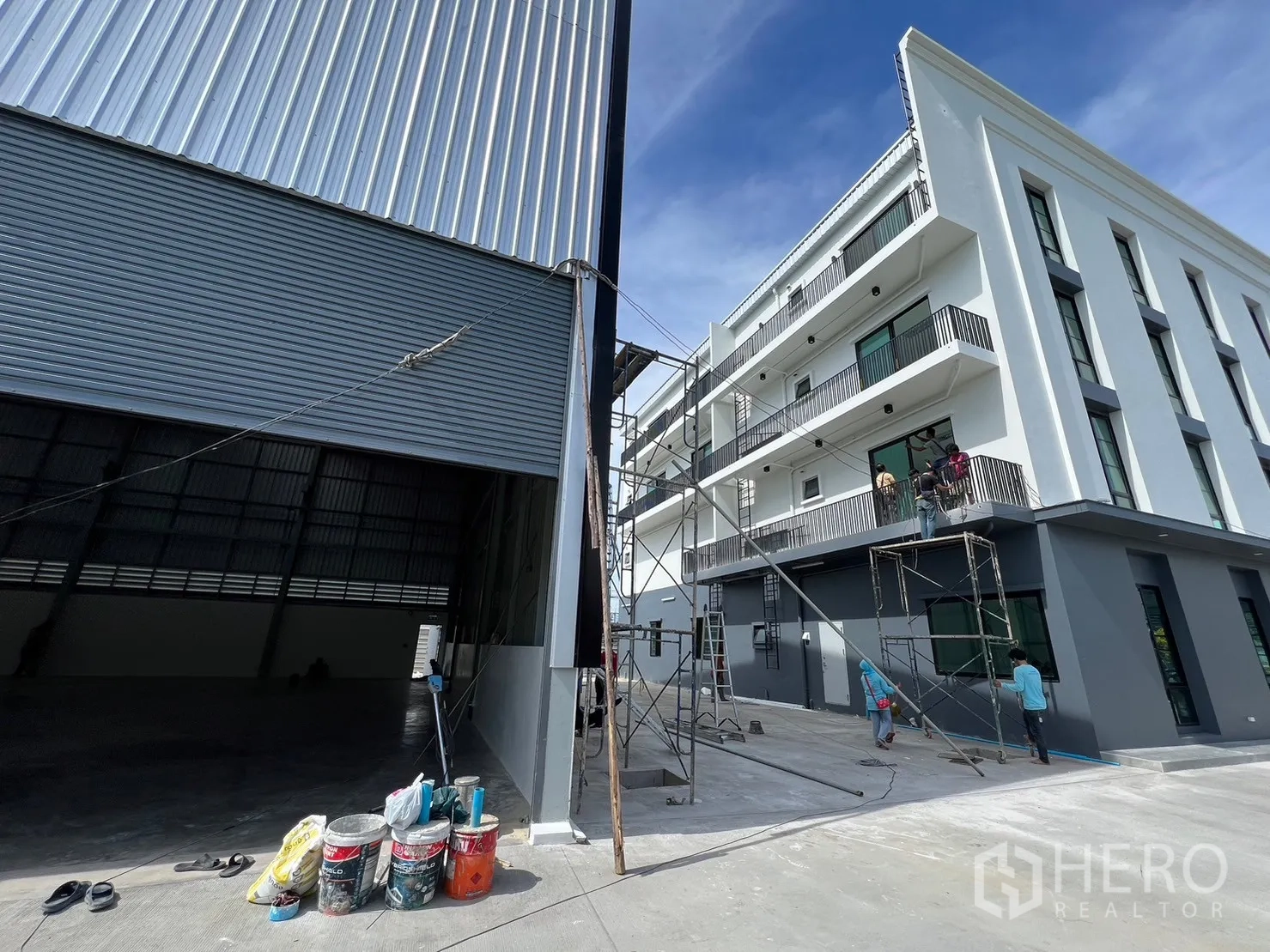 货栈 出租在Bang Sao Thong, Samut Prakan - 仓库装卸门旁的全新办公楼外立面，带阳台与脚手架。