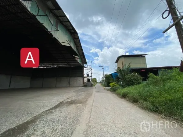 Factory for rent in Chachoengsao - Wide access road beside a large metal‑clad factory warehouse in Mueang Chachoengsao under a cloudy sky.