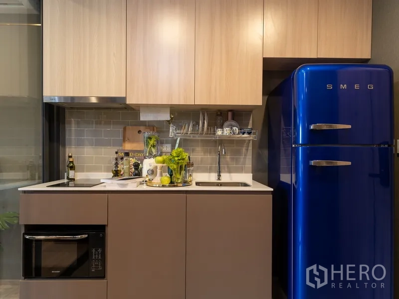 公寓 出售在Ratchathewi, Bangkok - 紧凑厨房，橱柜、灶台与水槽，配复古蓝色冰箱。