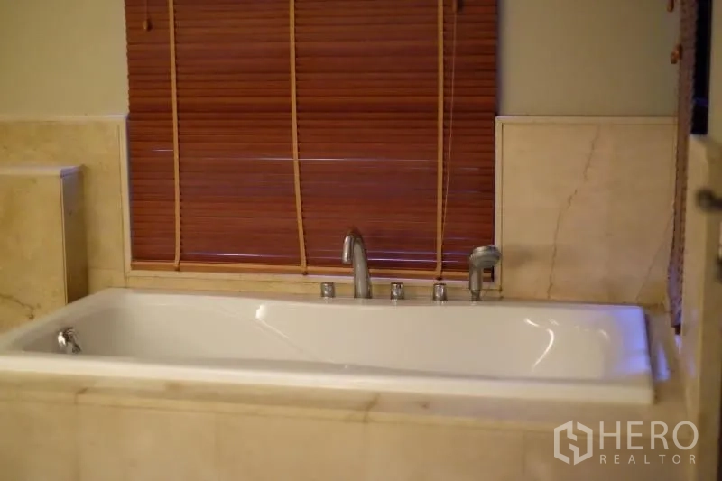 Condominium for rent in Watthana, Bangkok - Bathroom featuring a rectangular soaking bathtub with marble surround and wooden blinds.