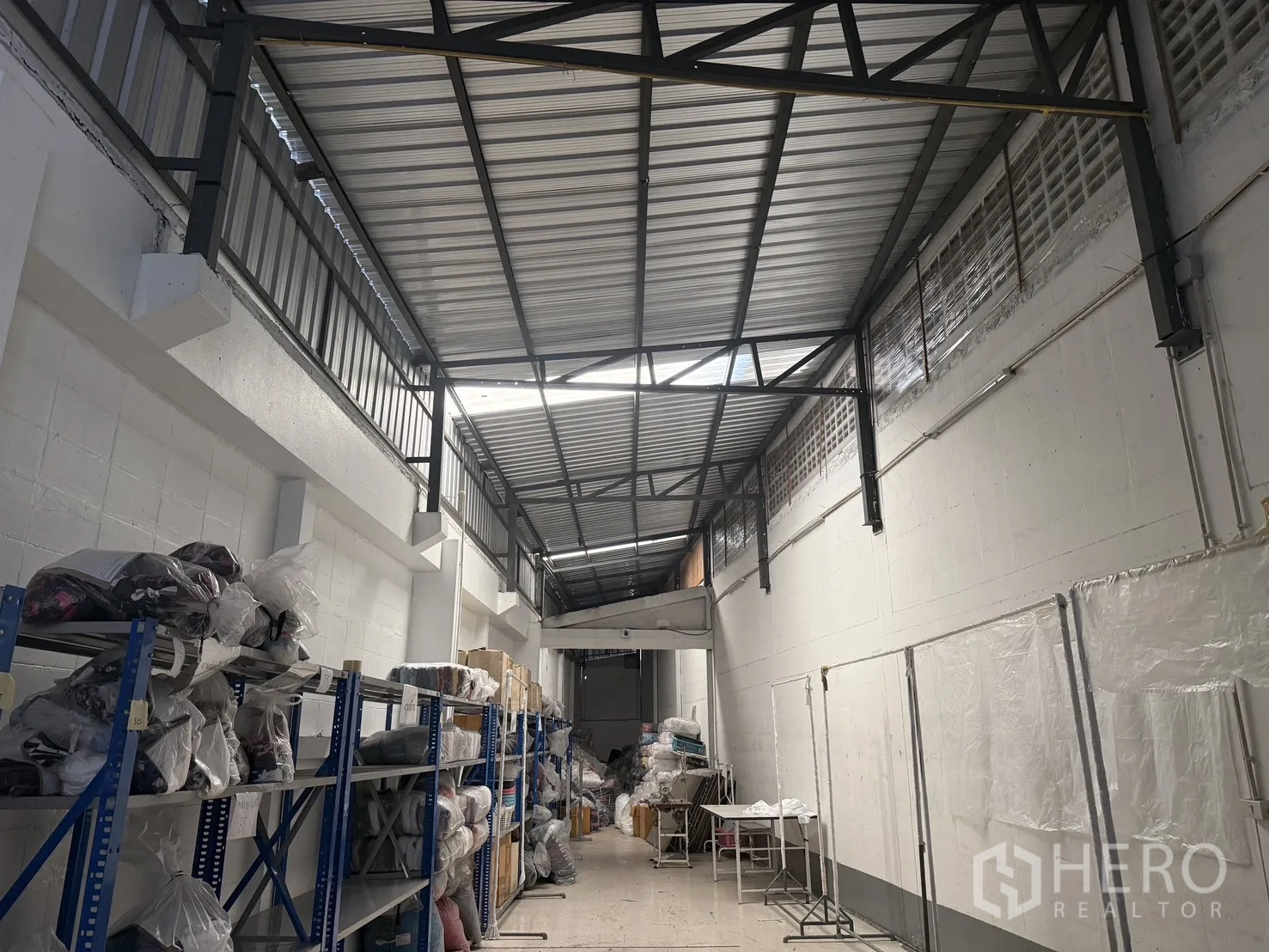 Warehouse for rent in Suan Luang, Bangkok - Warehouse interior with tall metal truss roof, block walls, steel shelving and an open central aisle.