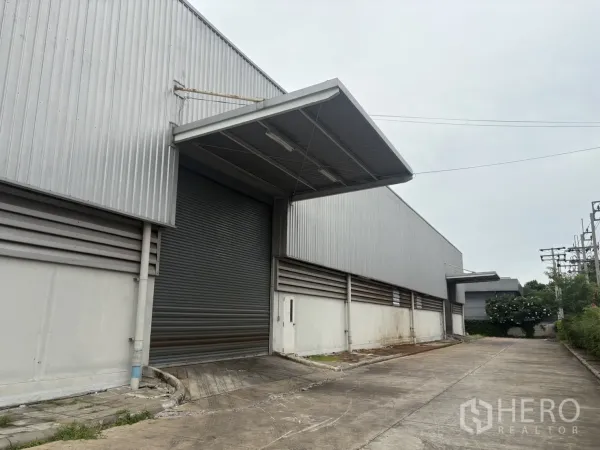 Factory for rent or sale in Samut Prakan - Covered loading bay with a roller shutter door on a corrugated metal warehouse wall.