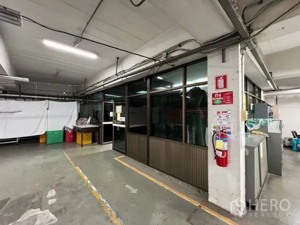 Warehouse for rent in Bang Kapi, Bangkok - Interior corner with glass-partition office, visible cabling and fire extinguisher in an industrial setting.